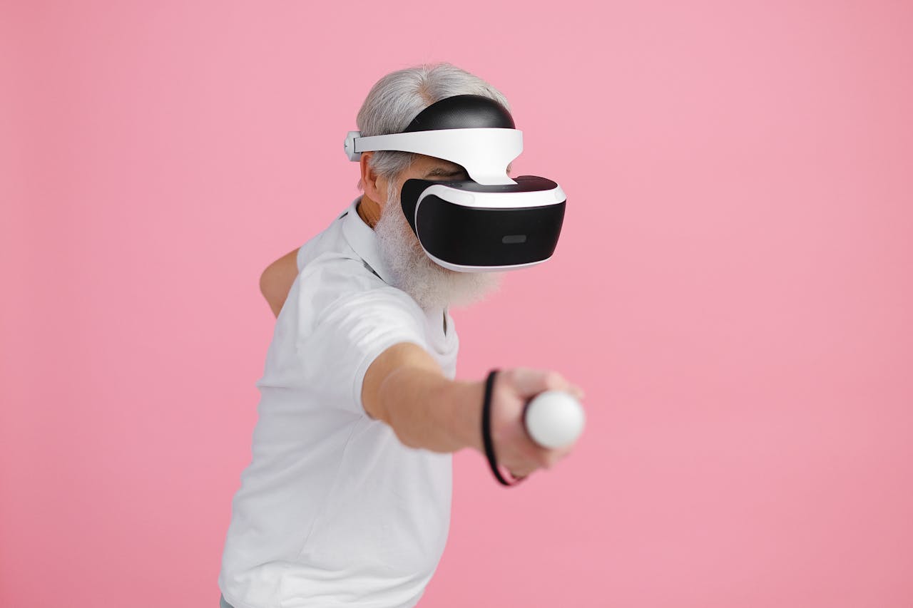 Senior man wearing VR headset and interacting with virtual environment against pink background.